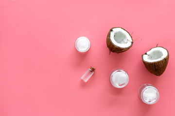 Fototapeta premium Cosmetics based on coconut oil. Oil in small bottle, cream, coconut pulp, half of coconut with shelf on pink background top view copy space