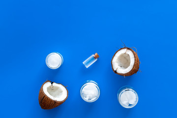 Coconut oil cosmetics for skin and hair care. Oil in small bottle, cream jar, halfs of coconut with shelf on blue background top view copy space