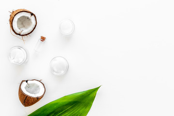 Coconut oil cosmetics for skin and hair care. Oil in small bottle, cream jar, halfs of coconut with shelf, palm leaves on white background top view copy space