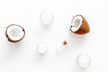 Coconut oil cosmetics for skin and hair care. Oil in small bottle, cream jar, halfs of coconut with shelf on white background top view