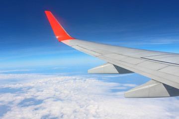 Wing of an airplane flying above the cloud looks from the window of the plane