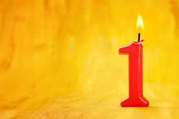 Red number one burning candle on a golden background with copyspace