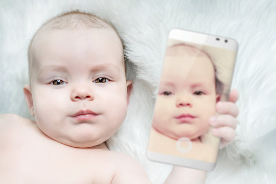 A cute baby is holding a smartphone with his photo