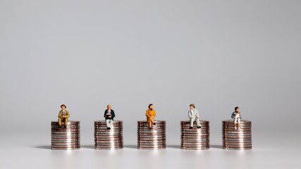 Economic problem concept for aging society and low birth rate. miniatures sitting on piles of coins