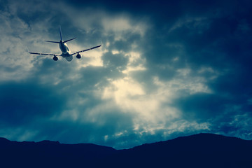 Fototapeta na wymiar An airplane flying through a dramatic raincloud sky over a mountain range in the horizon.