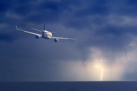 Passenger airplane flying above sea on stormy sky with dark clouds and lightnings.