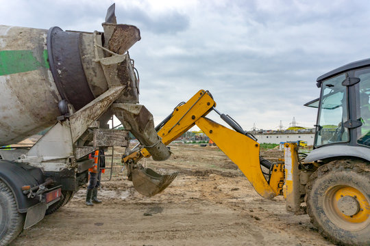 Concrete from a concrete mixer is poured into a bucket of an excavator