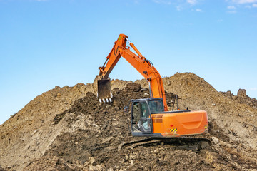 Excavator at the construction site pours a pile of soil