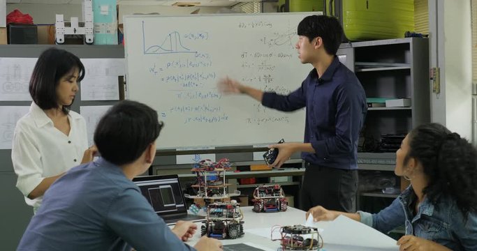 In Computer Science Class Teacher talking to students about robot technology. Male engineer present project with team. People with technology or innovation concept.