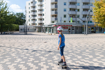 Ein 9 Jahre altes Mädchen skatet auf einem Skateboard auf einem Platz vor einem Hochhaus © Markus Wegmann