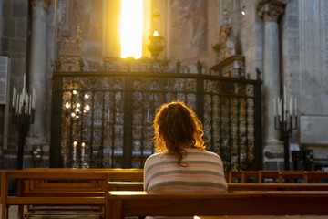 Woman praying alone in a cathedral, sitting in a beautiful ray of divine light