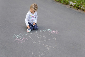 Preschool caucasian girl drawing a house with chalks on the pavement
