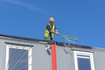 Worker at the construction site cleans the roof of the water with a brush