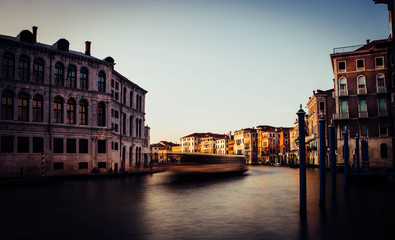 Naklejka premium A boat in motion crosses the Grand Canal of Venice at sunset, while the sun hits the face of some historic buildings on the banks of the canal