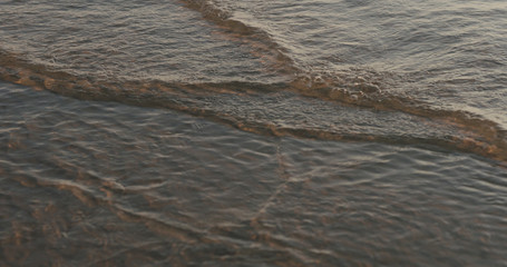 closeup of small waves with caustics on a beach at sunset