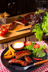 bbq spareribs on the plate with green salad and white sauce.