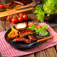 bbq spareribs on the plate with green salad and white sauce.