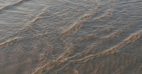 closeup of small waves with caustics on a beach at sunset