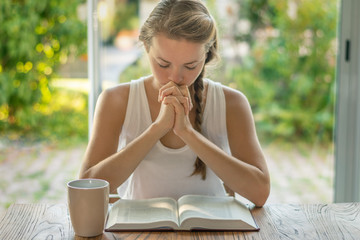 Christian worship and praise. A young woman is reading the Bible and praying in the early morning