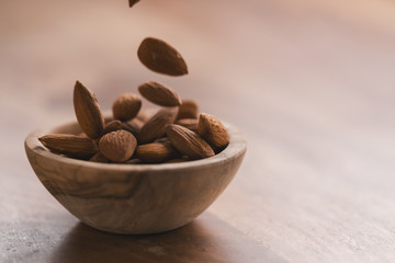 peeled almonds falling in wood bowl with copy space