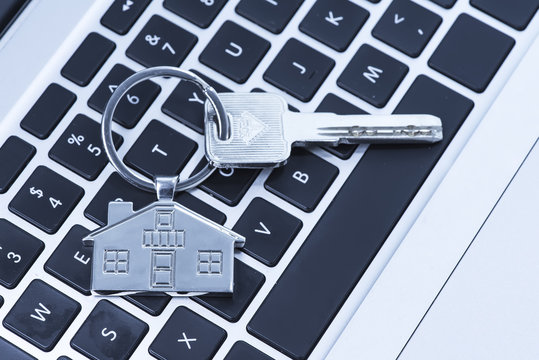 Key and keychain in the shape of a house on keyboard background.