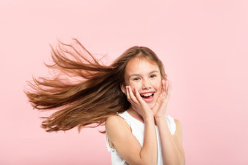 pretty and cute adolescent girl with hair flying in the wind. haircare products and beauty concept. portrait of young kid on pink background.