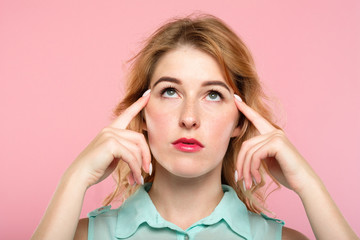 mind games telepathy thought transfer and brain power. beautiful girl concentrating on invisible object above her. index fingers on temples. young beautiful blond woman portrait on pink background. - obrazy, fototapety, plakaty