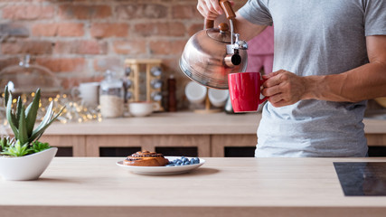 healthy food and quick breakfast. morning meal. poppy seed bun fresh and blueberry a kitchen table. man pouring boiling water from kettle to make tea in a red mug.