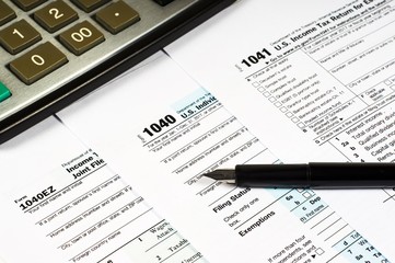 Tax Form 1040, 1041, 1040EZ and pen on a background of a calculator, close-up