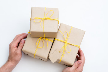 presents wrapped in a craft paper tied with a yellow twine. hands holding celebratory gifts or reward on festive holiday. packages on white background with copy space.