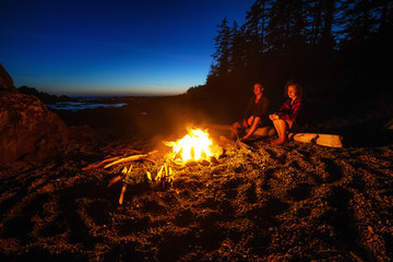 Couple friends are enjoying a camp fire on the beach during a vibrant summer sunset. Taken in...