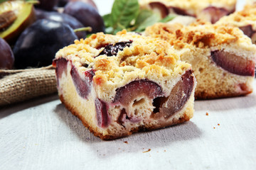 Rustic plum cake on wooden background with plums around.