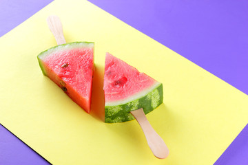 Watermelon pop art. Pieces of watermelon on stick on a yellow purple background. Natural dessert in a minimalist style. Creative story with food for vegan