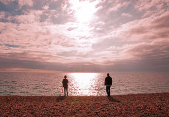 Two people stood looking at the ocean sunset.