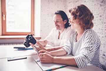 A middle-aged man and a young woman are sitting at a table, a camera and a diary. Training and master classes in photography and processing, education concept, creative professions