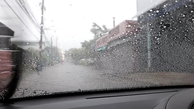 A look through the windshield of a car with working wipers at wet road. Traveling when is rain at street.