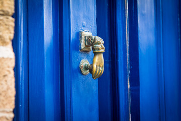 A copper door handle in the form of a hand on a wooden door in blue. Close-up. Moroccan style. Africa, Morocco, Essaouira