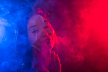 Obraz premium Portrait of asian woman smoking vape or e-cigarette in neon light at dark background.