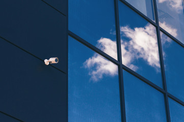 Glass facade of modern office building with security camera and reflected clouds