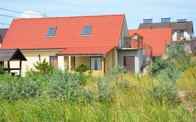 Cozy cottage house with red metal roof, balcony and attic window shylights.