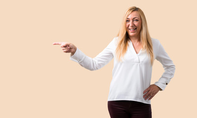 Middle age blonde woman with white shirt pointing finger to the side and presenting a product while...