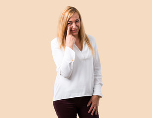 Middle age blonde woman with white shirt standing and looking to the front opening the eye with...