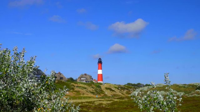 Leuchtturm H&ouml;rnum Sylt mit D&uuml;nen Landschaft  Reetdach H&auml;usern und  blauen Himmel
