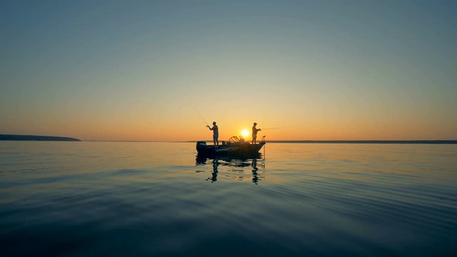 Male silhouettes while fishing from a motorboat during sunrise
