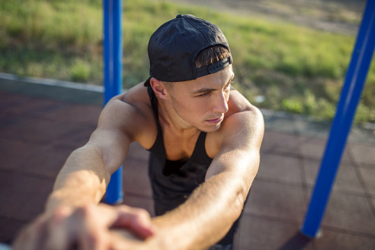 Closeup horizontal image of tired young muscular man relaxing after workout outdoors. Caucasian athlete man wears black sportswear relaxing after fitness workout exercises outside on sports ground.