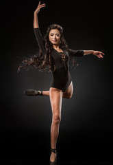Fototapeta na wymiar smiling ballerina in black bodysuit and ballet shoes dancing on dark backdrop