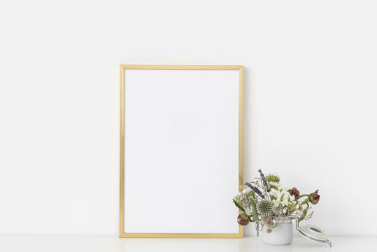 Gold a4 portrait frame mockup with dried field wild flowers in small white poton white wall background. Empty frame, poster mock up for presentation design.