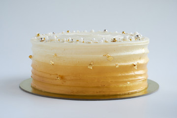 Cake with white cream, decorated with silver and gold confectionery sprinkles and gold leaf on a...