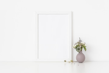 Elegant white a4 portrait frame mockup with dried field wild flowers in vase on white wall background. Empty frame, poster mock up for presentation design
