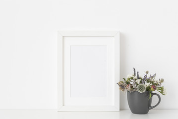 Molern white a5 portrait frame mockup with dried field wild flowers in mug on white wall background. Empty frame, poster mock up for presentation design. 
